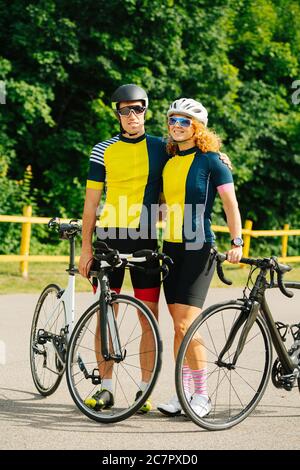 Nettes Radlerpaar posiert mit ihren Fahrrädern, trägt die gleichen Farben Stockfoto