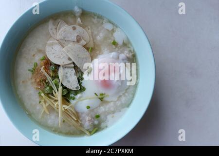 Congee. Belag mit weich gekochten Eiern, Schweinshaxe, Schweinewurst, gebratenem Knoblauch und Ingwer. Sehen Sie köstlich aus. Stockfoto