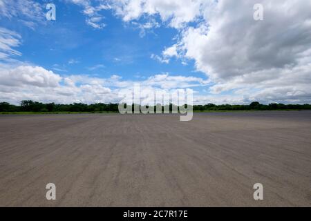 Leeren Sie den flachen Asphaltboden. Grüne Bäume am Horizont. Sonniger blauer Himmel mit herrlicher weißer Wolkenlandschaft. Weitwinkel Stockfoto