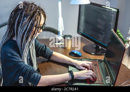 Moderne junge weibliche Programmierer ist das Schreiben von Programmcode auf einem Laptop zu Hause. Remote-Arbeit im IT-Bereich. Das Konzept der Softwareentwicklung. Stockfoto