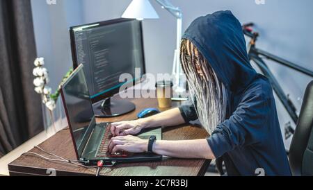 Frau Hacker in einer Haube sind die Programmierung von Virus-Code auf einem Laptop. Das Konzept des Internet-Betrugs und des Hacking von persönlichen Daten Stockfoto