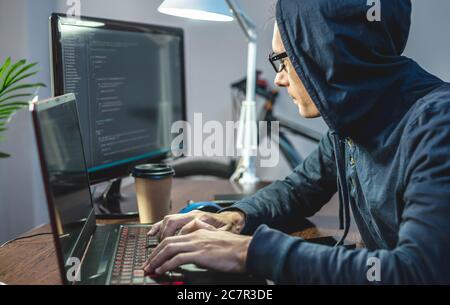 Mann Hacker in einer Haube sind die Programmierung von Virus-Code auf einem Laptop. Das Konzept des Internet-Betrugs und des Hacking von persönlichen Daten Stockfoto