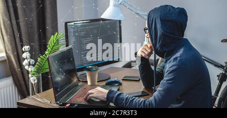 Mann Hacker in einer Haube sind die Programmierung von Virus-Code auf einem Laptop. Das Konzept des Internet-Betrugs und des Hacking von persönlichen Daten Stockfoto