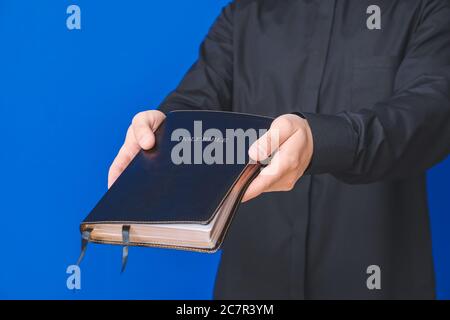 Junger Priester mit Bibel auf farbigem Hintergrund, Nahaufnahme Stockfoto