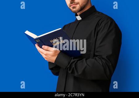 Junger Priester liest Bibel auf farbigem Hintergrund Stockfoto
