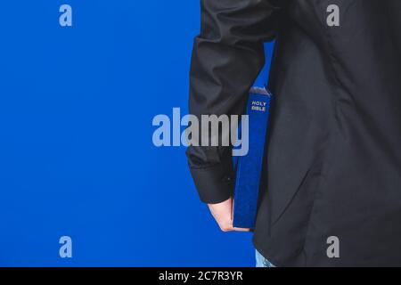 Junger Priester mit Bibel auf farbigem Hintergrund, Nahaufnahme Stockfoto