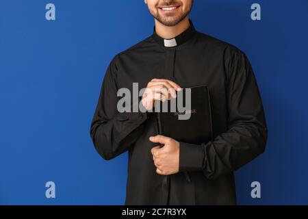 Junger Priester mit Bibel auf farbigem Hintergrund Stockfoto