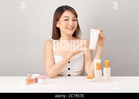 Junge asiatische Frau hält Hautpflege-Creme mit Smiley Gesicht isoliert auf weißem Hintergrund. Stockfoto