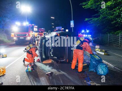 Reinbek, Deutschland. Juli 2020. Feuerwehrleute in Schutzanzügen untersuchen Flüssigkeiten, die nach einem Verkehrsunfall in einem Fahrzeug transportiert werden. Der stark betrunkene Fahrer des Autos hatte ein geparktes Auto getroffen, dann kippte sein Auto auf seine Seite. Der Mann wurde im Fahrzeug eingeschlossen und musste von der Feuerwehr befreit werden. Dabei entdeckten die Einsatzkräfte Buttersäure im Fahrzeug, die dann von den Einsatzdiensten mit speziellen Schutzanzügen aus dem Fahrzeug entfernt werden musste. Quelle: Daniel Bockwoldt/dpa/Alamy Live News Stockfoto