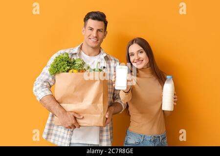 Paar mit Essen in der Tasche und Handy auf farbigem Hintergrund Stockfoto