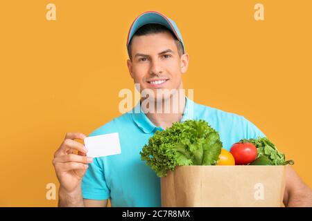 Lieferer mit Essen in Tasche und Visitenkarte auf farbigem Hintergrund Stockfoto