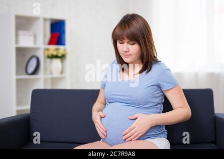 Porträt einer schwangeren jungen Frau, die zu Hause an Bauchschmerzen leidet Stockfoto