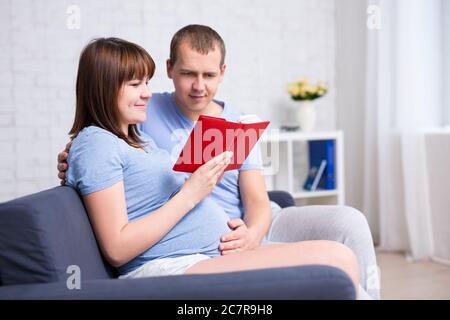 Junge schwangere Paar Buch im modernen Wohnzimmer lesen Stockfoto