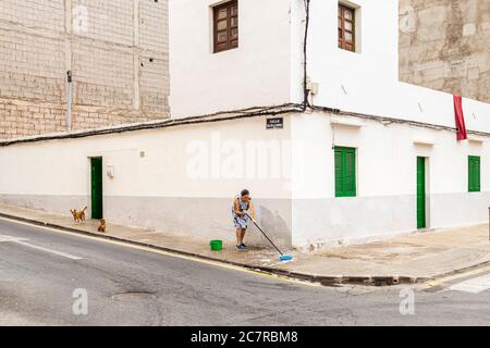 Ältere Frau, die sich den Fußweg vor ihrem Haus wascht, beobachtet von zwei Hunden in Playa San Juan, Teneriffa, Kanarische Inseln, Spanien Stockfoto