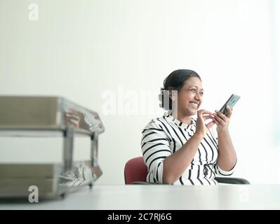 Glückliche indische Geschäftsfrau hinterlassen eine Sprachnachricht auf ihrem Handy. Büroumgebung. Stockfoto