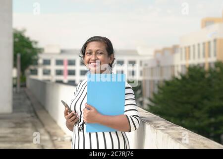 Porträt einer schönen lächelnden indischen Geschäftsfrau. Im Freien mit Bürogebäuden im Hintergrund. Stockfoto