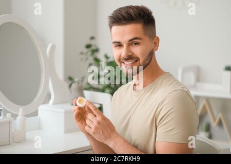 Schöner junger Mann mit Lippenbalsam zu Hause Stockfoto