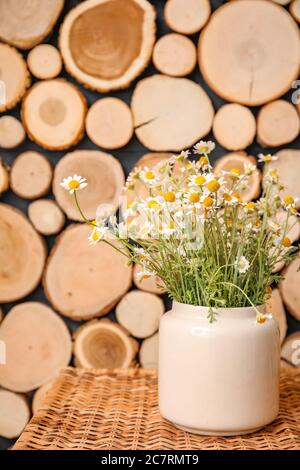 Vase mit schönen Kamillen auf Tisch neben Holzwand Stockfoto