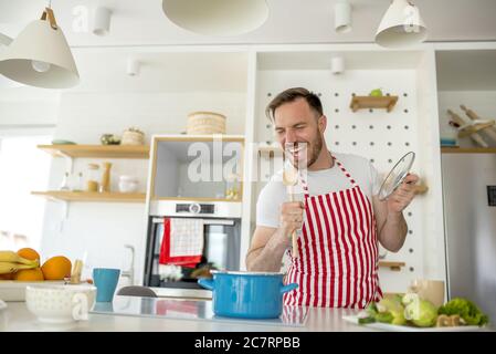 Mann trägt eine weiße Schürze mit roten Linien und Kochen Etwas in der Küche Stockfoto