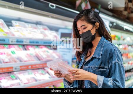 Junge asiatische Frau trägt schützende Gesicht Abdeckung Wahl Lebensmittel im Geschäft Stockfoto