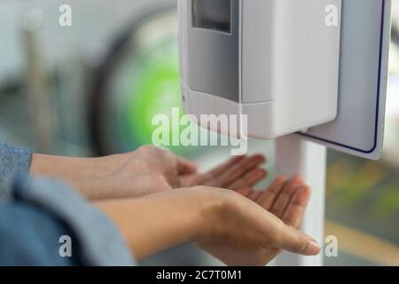 Nahaufnahme einer Frau, die die Hände unter der automatischen Desinfektionslösung hält Stockfoto