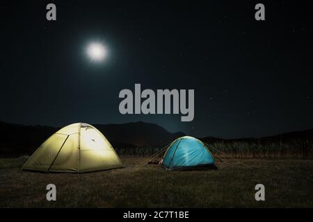 Camping in den Bergen unter dem Mond. Ein Zelt aufgeschlagen und unter dem Himmel glühend. Stockfoto