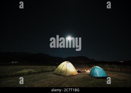 Camping in den Bergen unter dem Mond. Ein Zelt aufgeschlagen und unter dem Himmel glühend. Stockfoto