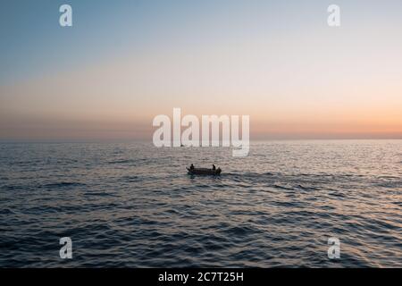 Schönes Meer mit Sonnenuntergang Himmel und Sonne durch die Wolken über. Segelboot mit Menschen fischen. Ruhige Meereslandschaft. Horizont über dem Wasser. Stockfoto