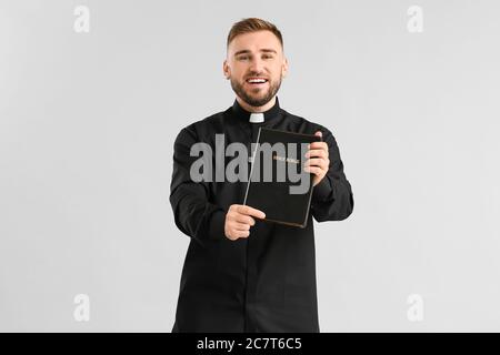 Schöner junger Priester mit Bibel auf hellem Hintergrund Stockfoto