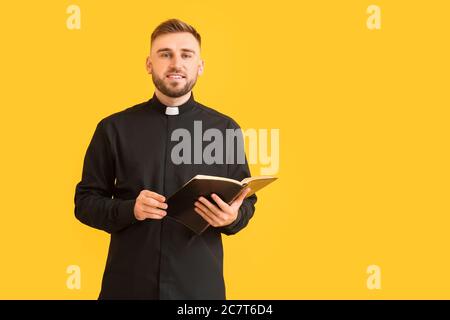 Schöner junger Priester mit Bibel auf farbigem Hintergrund Stockfoto