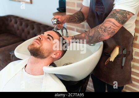 High-Angle-Ansicht eines Friseurs mit Tattoos waschen die Haare eines jungen männlichen Kunden Stockfoto