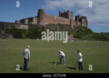 Der Bamburgh Cricket Club (Rückseite) spielt ihr erstes Cricket-Spiel seit der 19. Runde gegen die Ritter von Belmont, Durham, unter den Mauern von Bamburgh Castle in Northumberland. Stockfoto