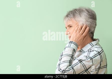 Ältere Frau mit Ohrenschmerzen auf farbigem Hintergrund Stockfoto