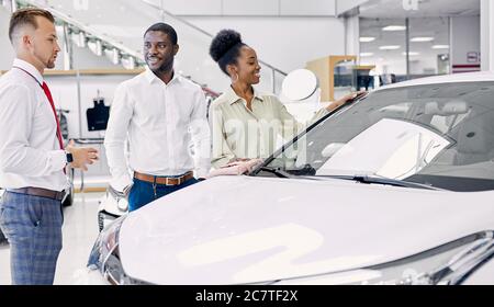 Schöne schwarze Afro-Paar aufmerksam zuhören Berater in Autohaus, selbstbewusste Verkäufer spricht über Vorteile und Eigenschaften des Autos sie Stockfoto