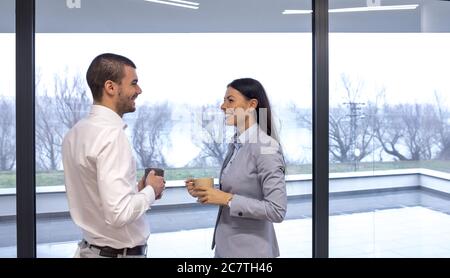Lächelnde Kollegen, die während der Kaffeepause ein Gespräch führen Steht in der Nähe des Fensters Stockfoto