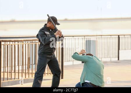 Aggressiver afroamerikanischer Polizist, der Menschen im Freien misshandelt Stockfoto