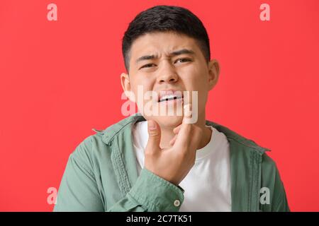 Asiatischer Mann mit kalten Wunde Anwendung Salbe auf seine Lippen vor Farbhintergrund Stockfoto