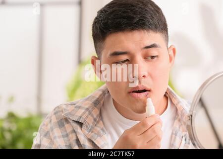 Asiatischer Mann mit kalten Wunde Anwendung Salbe auf seine Lippen Stockfoto