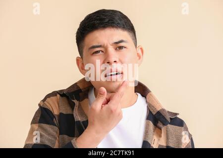 Asiatischer Mann mit kalten Wunde Anwendung Salbe auf seine Lippen vor Farbhintergrund Stockfoto