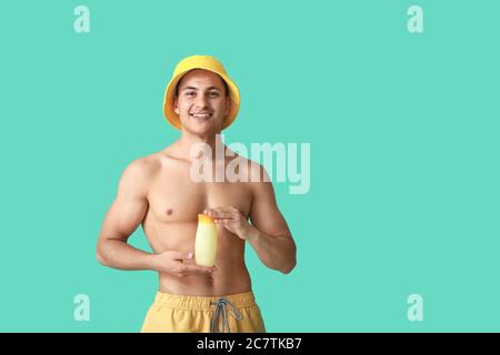 Fröhlicher junger Mann mit Sonnenschutzcreme auf farbigem Hintergrund Stockfoto