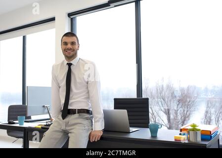 Junger Unternehmer, der sich im Büro auf seinen Schreibtisch stützt Stockfoto