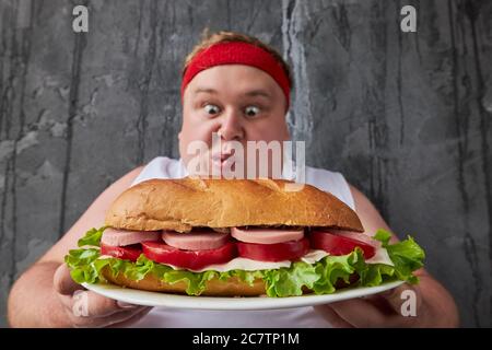 Gut aussehende kaukasischen dicken Mann gehen zu essen große leckere Sandwich, er ist nicht durch sein Übergewicht peinlich, er eata, was er will Stockfoto