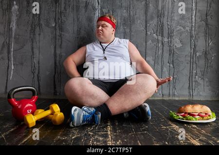Fat serious kaukasischen Mann weigert sich Junk ungesunde Lebensmittel, wollen Gewicht zu verlieren, schauen Sie sich Hanteln Stockfoto