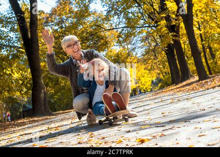 Großmutter und ihre Enkelin sitzen auf einem Skateboard und haben Spaß in einem Park Stockfoto