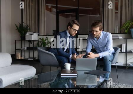 Seriöse männliche Kollegen kooperieren, diskutieren Ideen mit Laptop Stockfoto