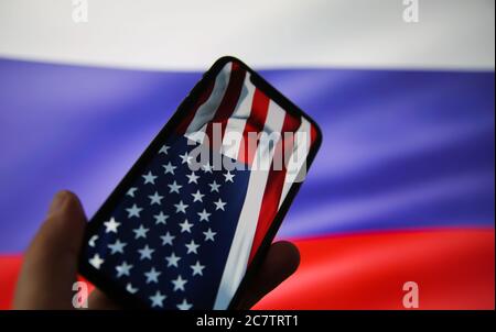 Viersen, Deutschland - 9. Juli. 2020: Ansicht auf der Hand halten Handy mit USA Flagge. Flagge von Russland Hintergrund. (Fokus auf den oberen Teil der amerikanischen Flagge) Stockfoto