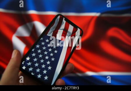 Viersen, Deutschland - 9. Juli. 2020: Ansicht auf der Hand halten Handy mit USA Flagge. Flagge von Nordkorea Hintergrund. (Schwerpunkt auf den oberen Teil der amerikanischen Fla Stockfoto