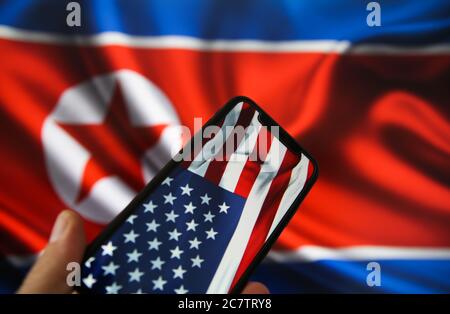 Viersen, Deutschland - 9. Juli. 2020: Ansicht auf der Hand halten Handy mit USA Flagge. Flagge von Nordkorea Hintergrund. (Schwerpunkt auf den oberen Teil der amerikanischen Fla Stockfoto