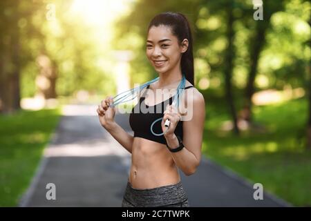 Fit lächelnd asiatische Frau posiert mit Springseil im Freien Stockfoto