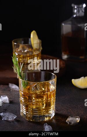 Drei Gläser kalter Whiskey mit Rosmarin, Zitronenschalen auf dunkelbraunem Hintergrund. Vertikale Ausrichtung. Stockfoto